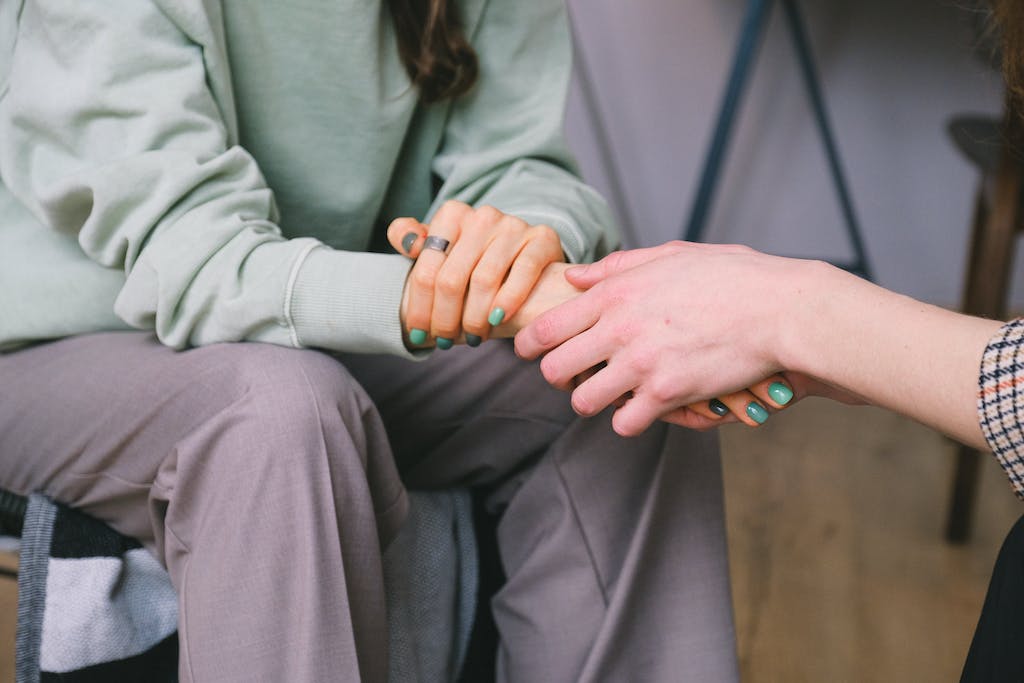 Eine Frau hält die Hand einer anderen Frau, während sie in einer Arise Bildungswerk-Sitzung auf einem Stuhl sitzt und sich auf die Förderung von Bildung und Werten konzentriert.